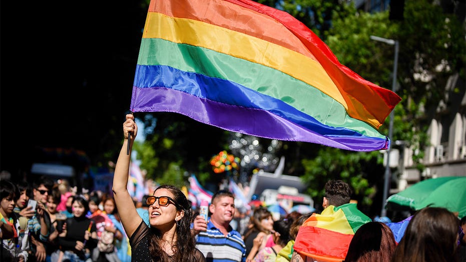 A woman at an LGBTQ pride parade, holding up a rainbow flag.